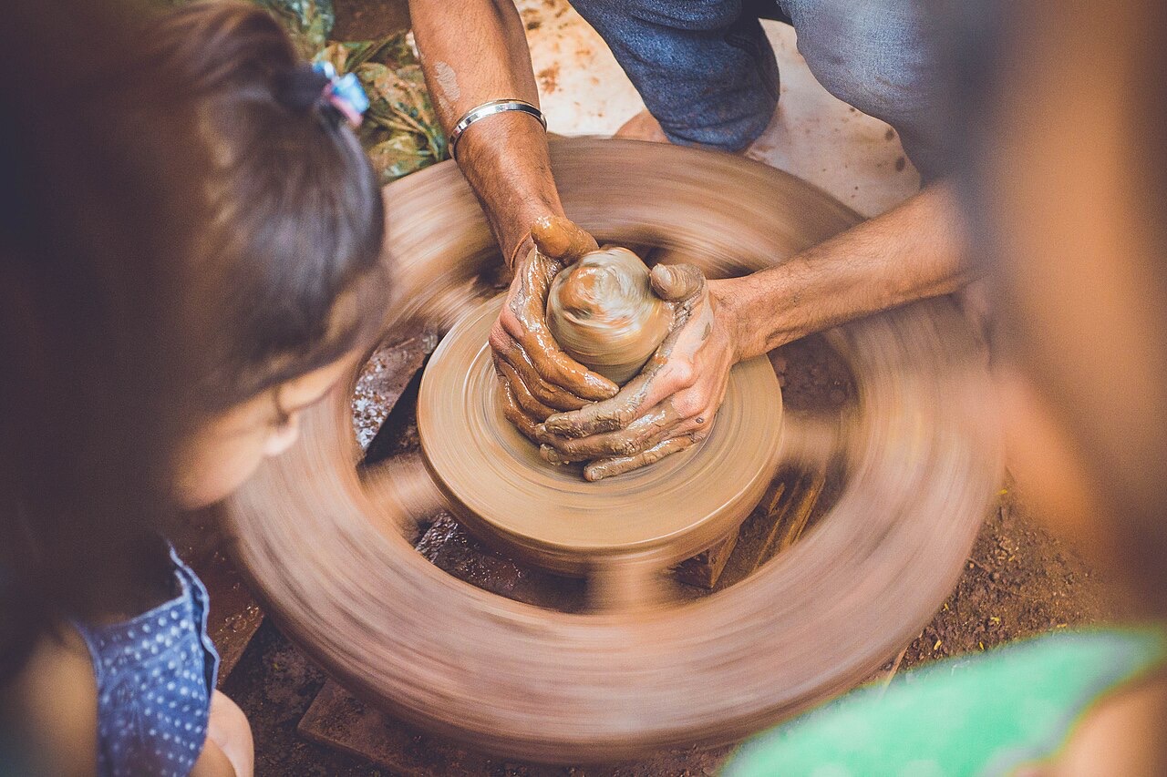 Friends shaping clay together on a wheel